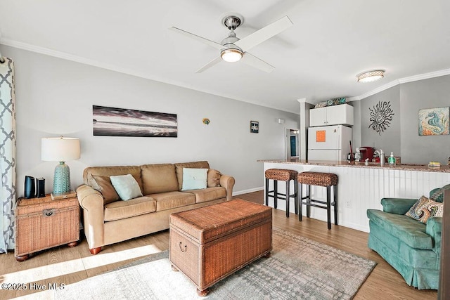 living room featuring crown molding, a ceiling fan, baseboards, and light wood finished floors