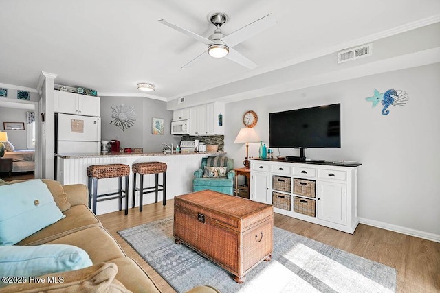 living room with baseboards, visible vents, ceiling fan, light wood-style floors, and crown molding