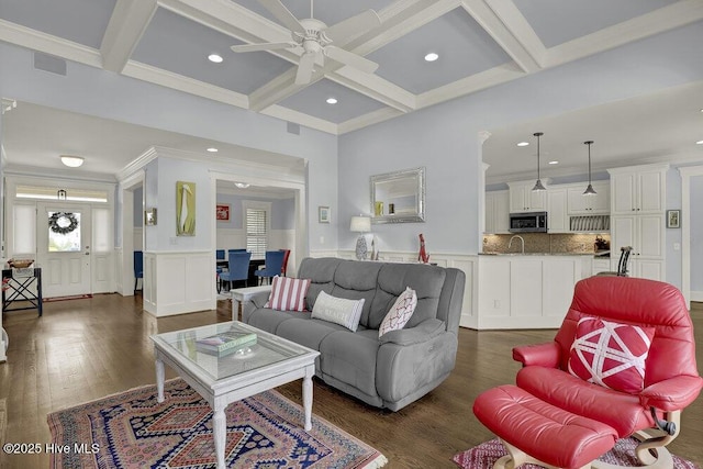 living room with ceiling fan, beamed ceiling, a wainscoted wall, dark wood-style floors, and coffered ceiling