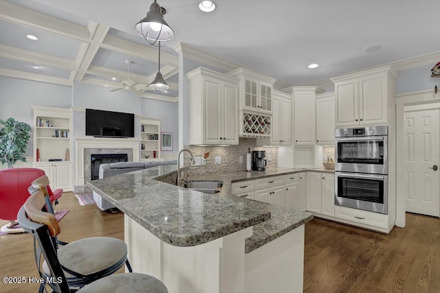 kitchen featuring coffered ceiling, a peninsula, ceiling fan, a sink, and double oven