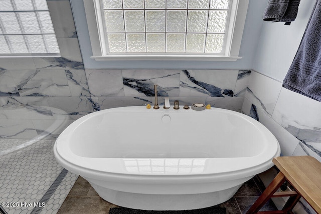 bathroom featuring tile walls, a freestanding tub, and a healthy amount of sunlight