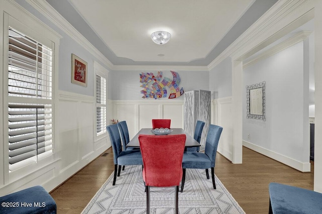 dining area featuring a decorative wall, wood finished floors, wainscoting, and ornamental molding