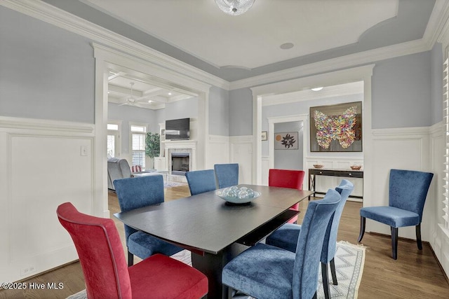 dining space with beamed ceiling, wainscoting, a fireplace, wood finished floors, and coffered ceiling