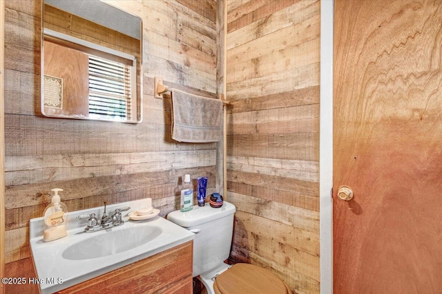 bathroom featuring wood walls, toilet, and vanity