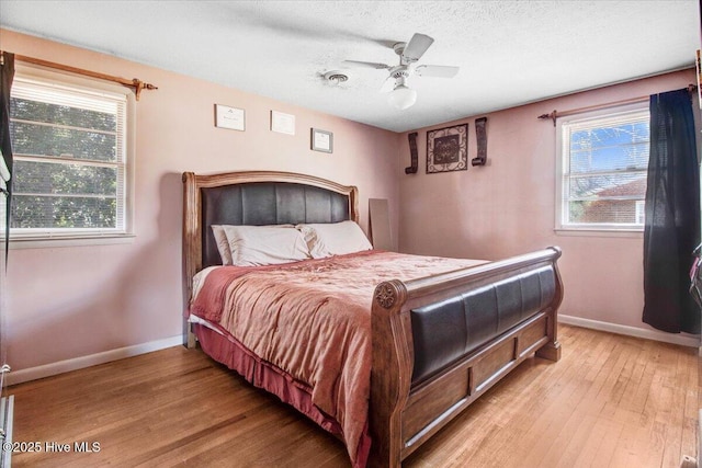 bedroom with baseboards, multiple windows, a textured ceiling, and light wood finished floors