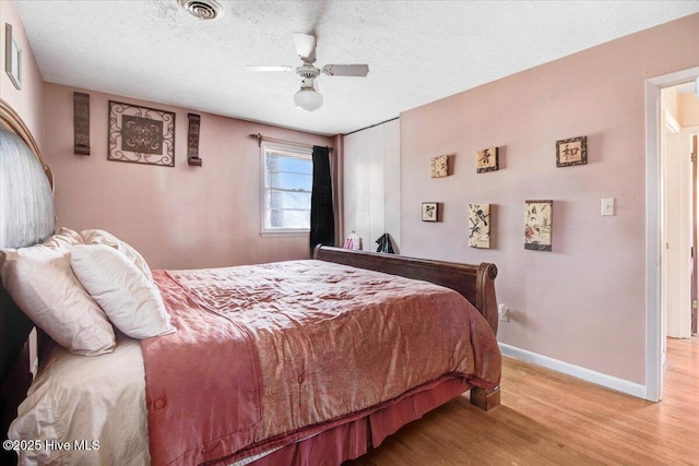 bedroom with wood finished floors, visible vents, baseboards, ceiling fan, and a textured ceiling