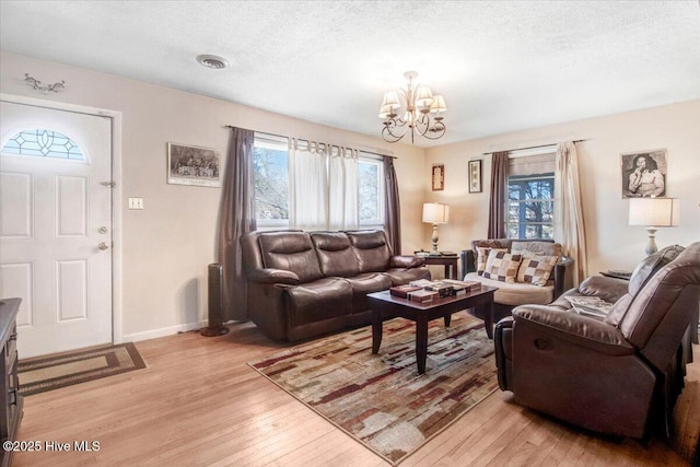 living area featuring visible vents, baseboards, a textured ceiling, a notable chandelier, and light wood-type flooring