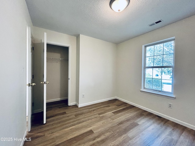 unfurnished bedroom with visible vents, a textured ceiling, baseboards, and wood finished floors