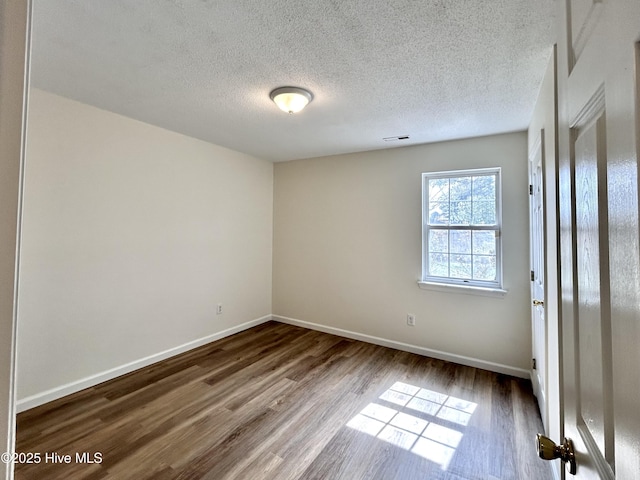 empty room with visible vents, a textured ceiling, baseboards, and wood finished floors