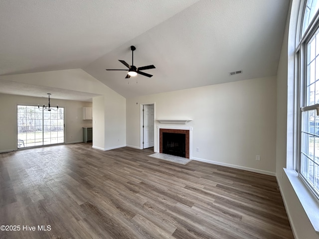 unfurnished living room with visible vents, dark wood-type flooring, a fireplace with flush hearth, vaulted ceiling, and ceiling fan with notable chandelier