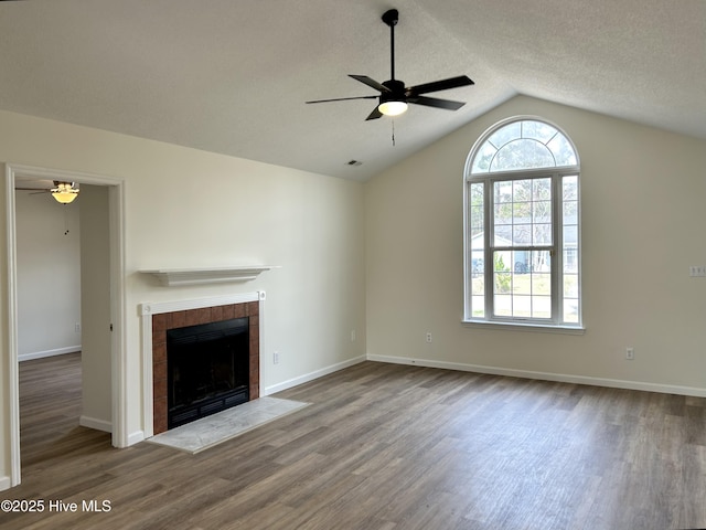 unfurnished living room with a ceiling fan, vaulted ceiling, wood finished floors, and a tile fireplace