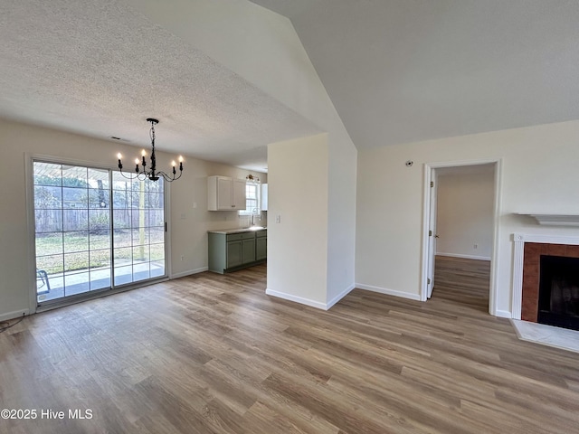 unfurnished living room featuring a tiled fireplace, an inviting chandelier, baseboards, and light wood finished floors