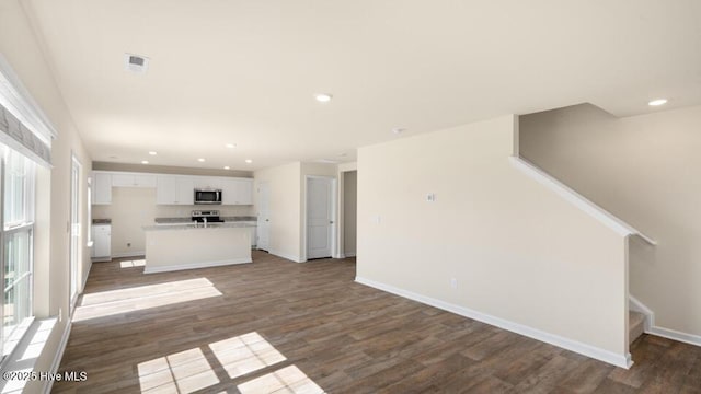 unfurnished living room featuring recessed lighting, baseboards, wood finished floors, and stairs