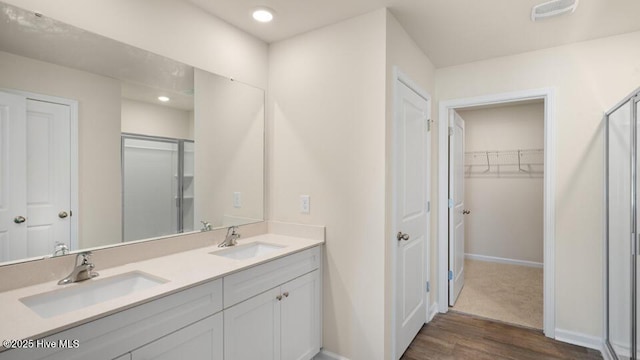 bathroom featuring double vanity, a stall shower, wood finished floors, and a sink