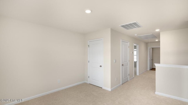 empty room with light carpet, visible vents, attic access, and baseboards