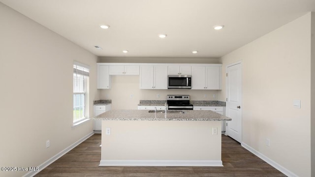 kitchen with dark wood finished floors, appliances with stainless steel finishes, white cabinetry, and a kitchen island with sink