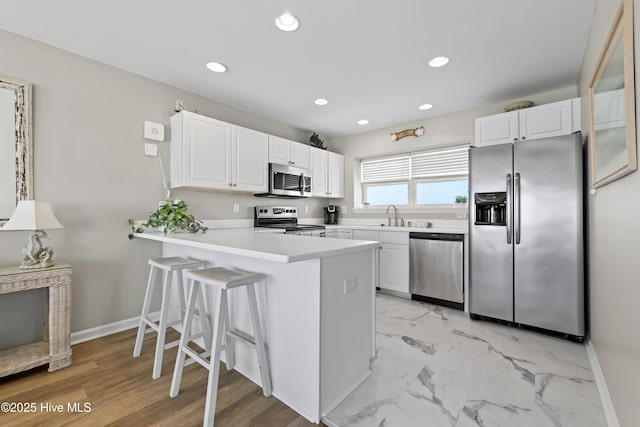 kitchen with a peninsula, recessed lighting, a sink, stainless steel appliances, and white cabinetry