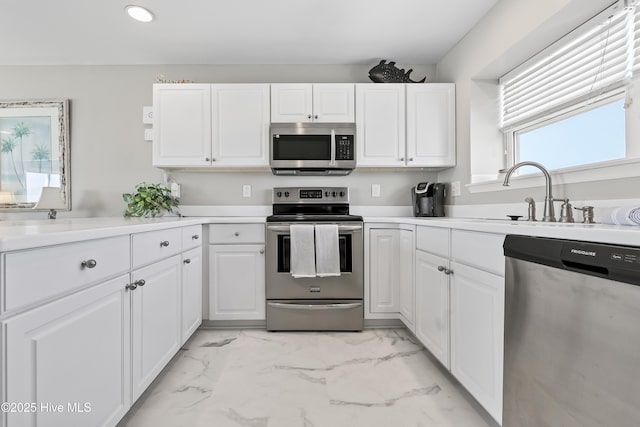 kitchen with white cabinetry, a sink, marble finish floor, and stainless steel appliances