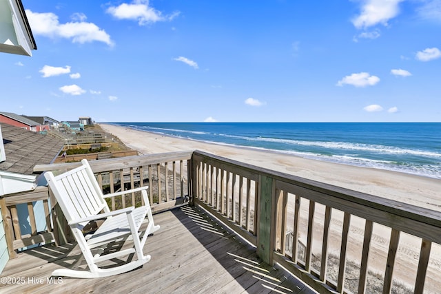 wooden terrace featuring a beach view and a water view