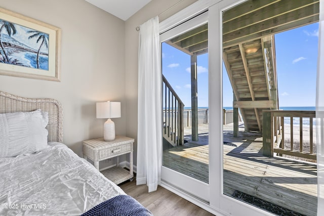 bedroom featuring access to exterior, wood finished floors, and a water view