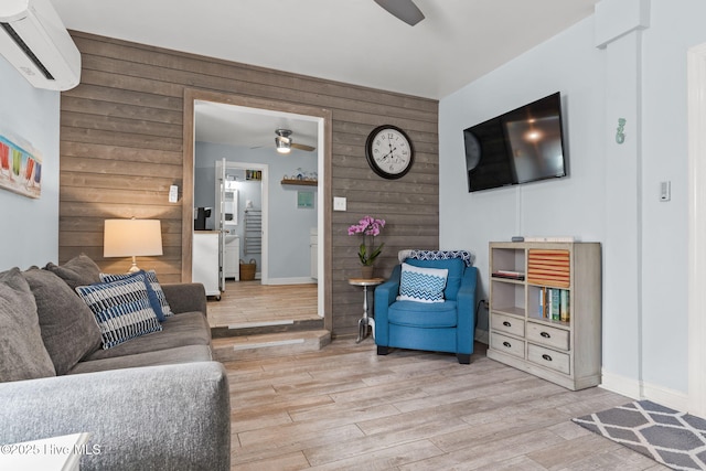 living area featuring a wall mounted AC, wooden walls, light wood-type flooring, baseboards, and ceiling fan