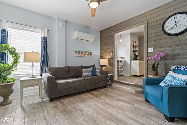 living area featuring light wood-style flooring, wooden walls, a wall mounted air conditioner, and ceiling fan