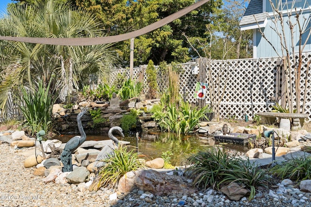 view of yard featuring fence and a garden pond