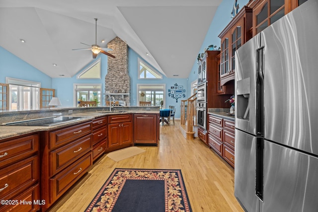 kitchen with stone counters, light wood-style flooring, stainless steel refrigerator with ice dispenser, black electric cooktop, and a sink