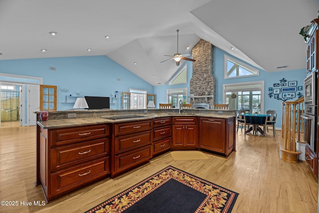 kitchen featuring light wood-style flooring, a sink, open floor plan, reddish brown cabinets, and a fireplace