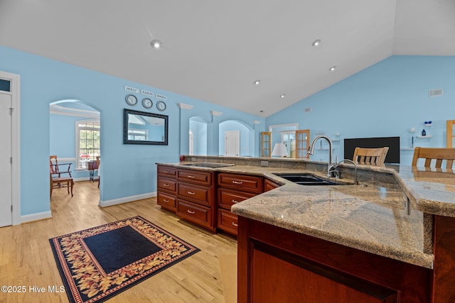 kitchen with black electric cooktop, light wood-style floors, arched walkways, and a sink