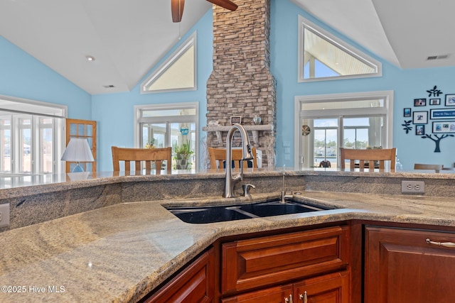 kitchen with vaulted ceiling, brown cabinets, visible vents, and a sink