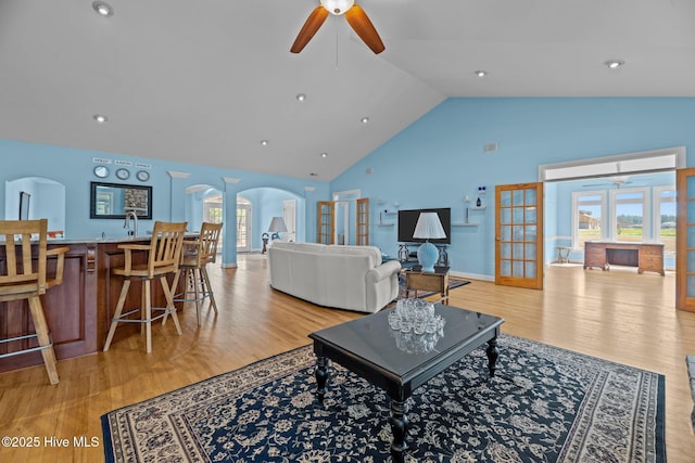 living area with arched walkways, light wood-style flooring, high vaulted ceiling, and ceiling fan