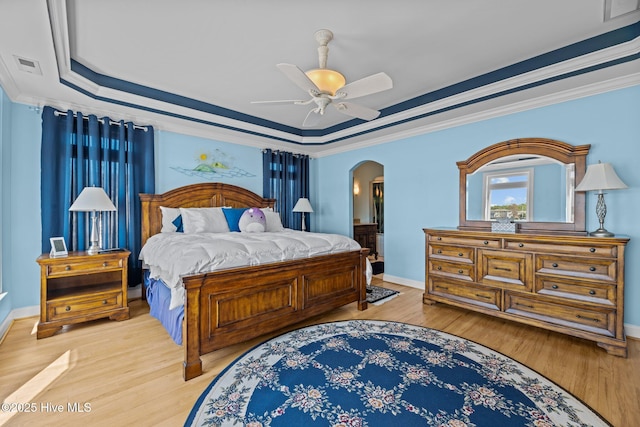 bedroom with visible vents, ornamental molding, light wood-style flooring, arched walkways, and a raised ceiling