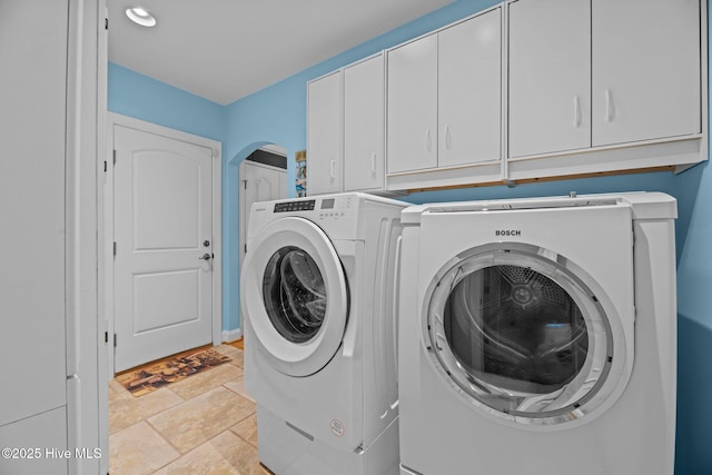 clothes washing area with arched walkways, cabinet space, washer and dryer, and stone finish flooring