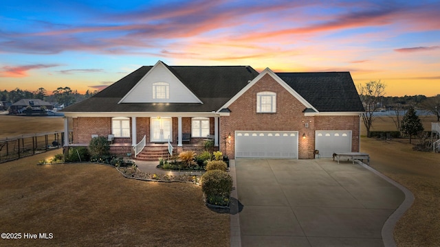 view of front of home with brick siding, fence, a front yard, covered porch, and driveway