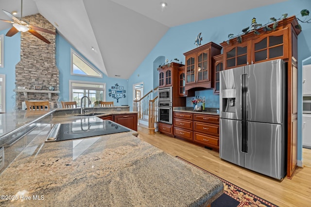 kitchen with high vaulted ceiling, a sink, appliances with stainless steel finishes, light wood finished floors, and glass insert cabinets