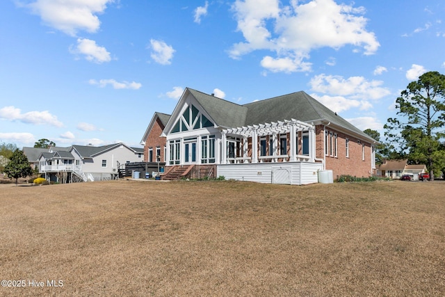 rear view of property featuring brick siding, a lawn, and a pergola