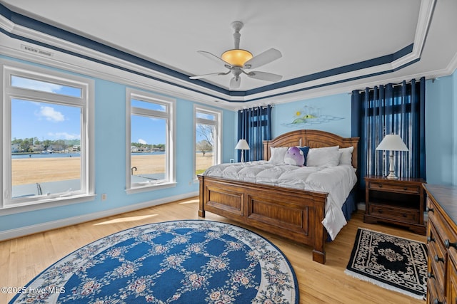 bedroom featuring a tray ceiling, light wood-style floors, crown molding, and a ceiling fan