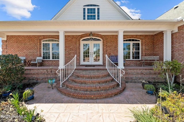 view of exterior entry featuring brick siding, french doors, and a porch