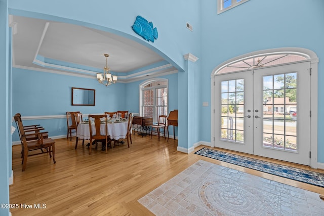 entrance foyer with a healthy amount of sunlight, light wood finished floors, arched walkways, a raised ceiling, and a notable chandelier