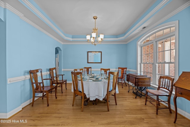 dining space featuring a raised ceiling, light wood-style flooring, arched walkways, and a chandelier