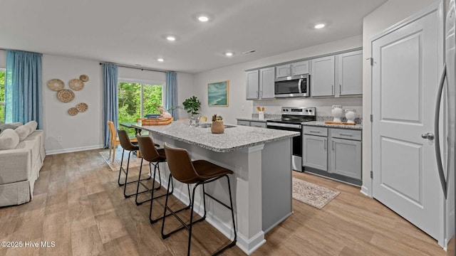 kitchen featuring gray cabinets, appliances with stainless steel finishes, a breakfast bar, and a kitchen island with sink