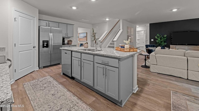 kitchen with gray cabinetry, a sink, open floor plan, light wood-style floors, and appliances with stainless steel finishes