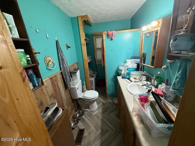 bathroom featuring a wainscoted wall, toilet, vanity, a stall shower, and a textured ceiling