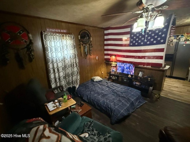 bedroom with a ceiling fan, wooden walls, wood finished floors, and stainless steel refrigerator with ice dispenser