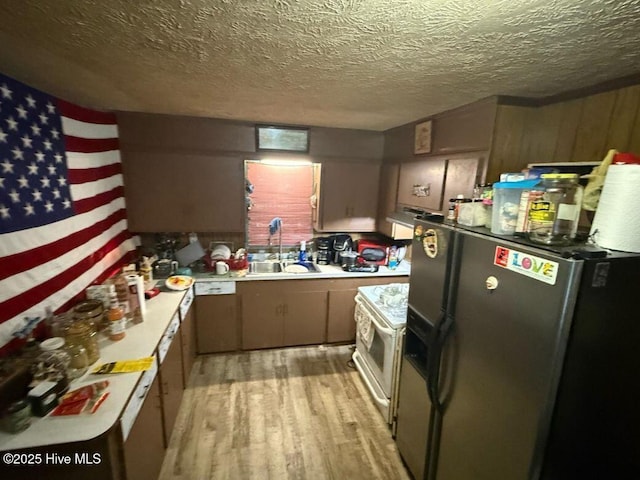 kitchen featuring white range with electric cooktop, a sink, light countertops, light wood-style floors, and refrigerator with ice dispenser