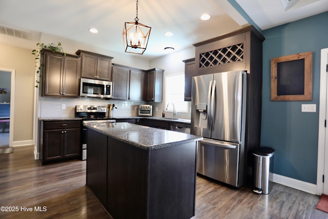 kitchen with a sink, dark brown cabinetry, dark wood-type flooring, appliances with stainless steel finishes, and tasteful backsplash