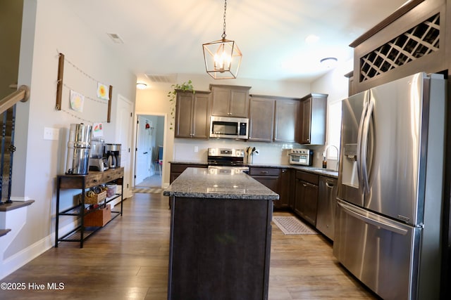 kitchen with a kitchen island, dark stone countertops, appliances with stainless steel finishes, wood finished floors, and a sink