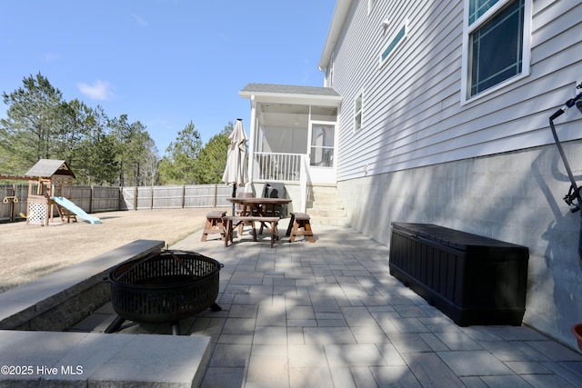 view of patio with a fire pit, a playground, a fenced backyard, a sunroom, and outdoor dining space