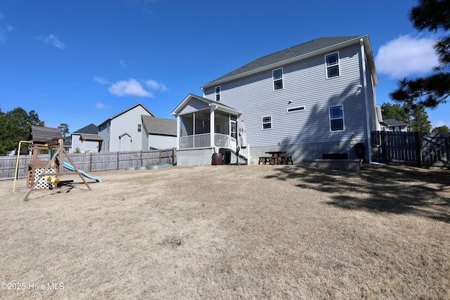 rear view of property with a playground, a fenced backyard, and a sunroom